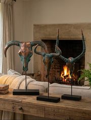 Decorative ram heads on stands in a living room with a fireplace and lamp.